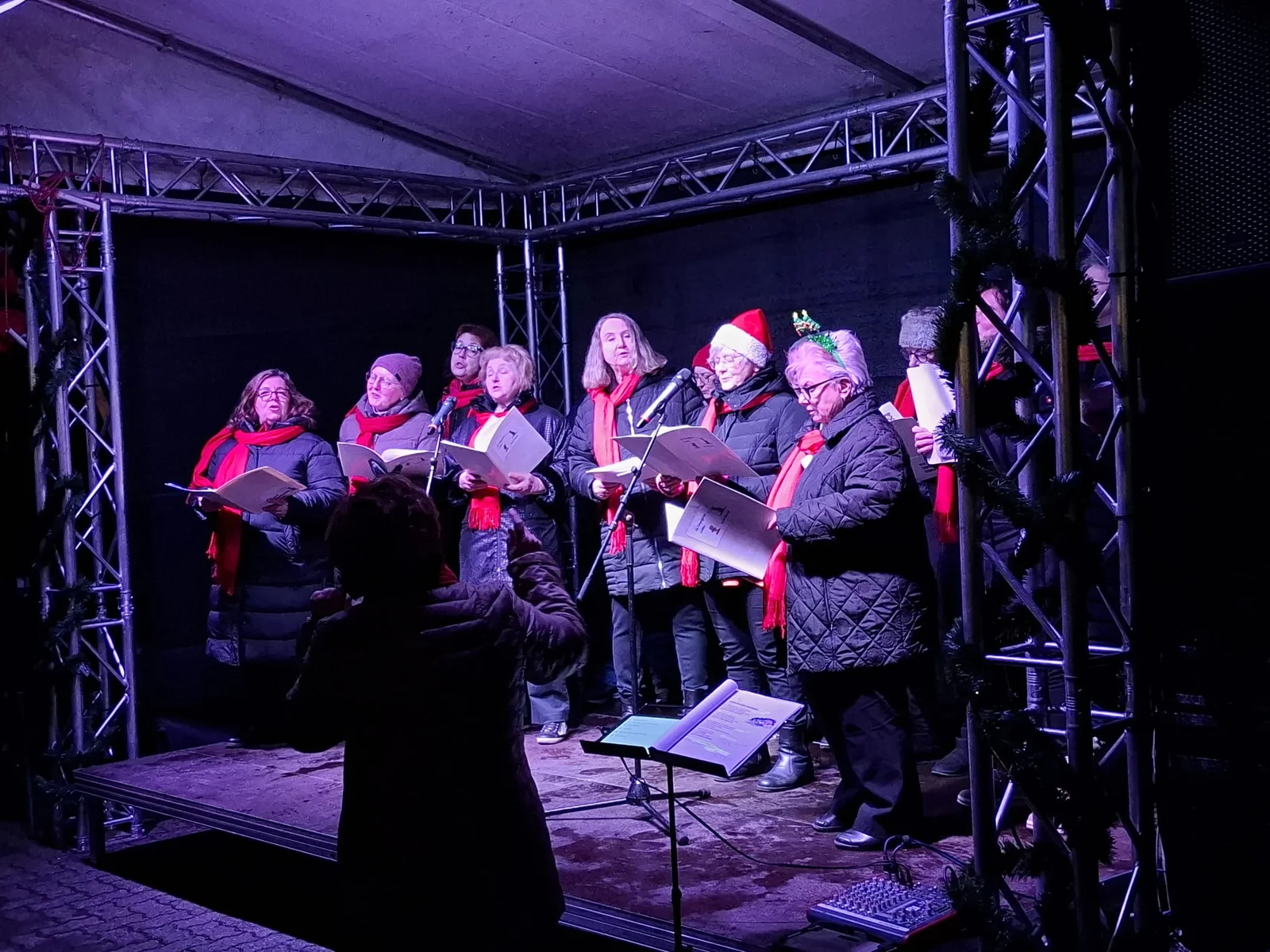 Chor mit roten Schals und Notenmappen auf einer weihnachtlich beleuchteten Bühne