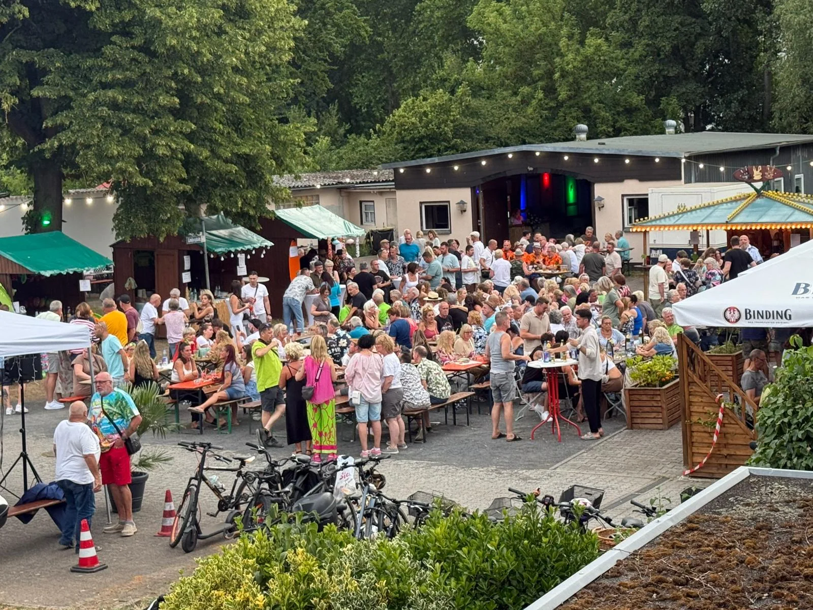 Gäste sitzen beim Sommerfest gemeinsam an langen Tischen auf dem Vereinsgelände