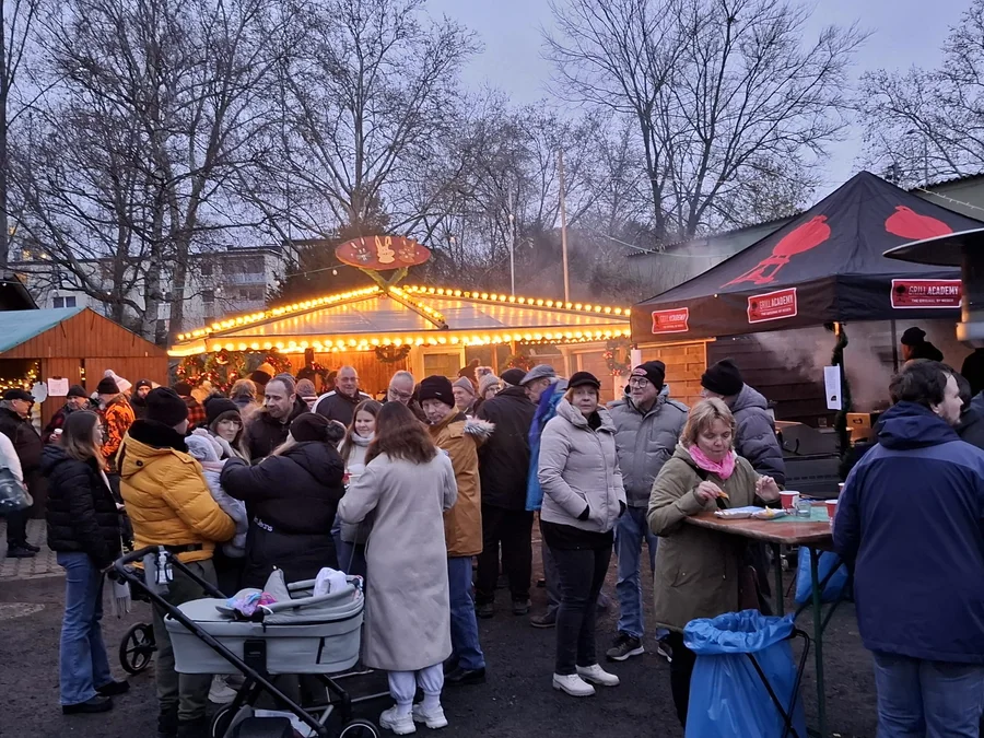 Wintergäste zwischen beleuchteten Ständen eines früheren Weihnachtsmarkts